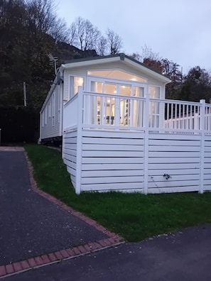 A white, single-story building with a balcony and a fenced area. - Haven Caravan Sleeps 6 Pet Friendly (New Quay)