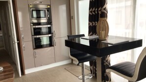 Una cocina compacta con electrodomésticos integrados, un comedor con una mesa negra y dos sillas, y un florero decorativo sobre la mesa.