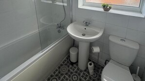 Un baño con bañera, lavamanos e inodoro. Hay una ventana con una planta en el alféizar.
