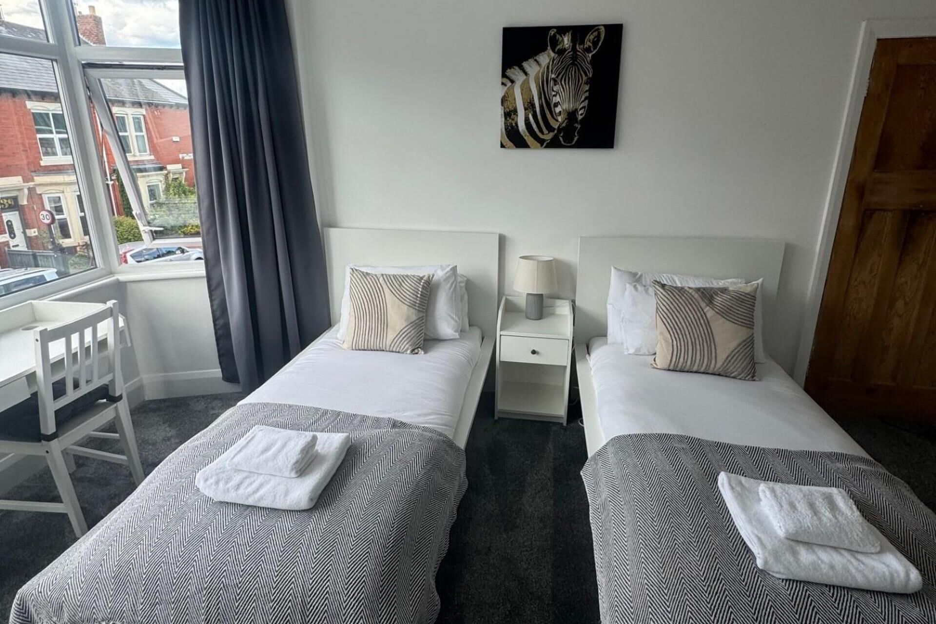 Ett hotellrum med två separata sängar, ett skrivbord och ett fönster med utsikt över byggnader.