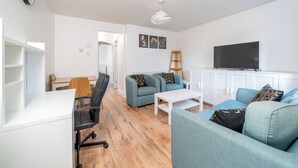 A modern living room with a white sofa, a blue sofa, a white coffee table, a black office chair, a wooden ladder, and a flat-screen TV mounted on the wall. - Crawley Stainer 1-bedroom With Parking and Garden (Crawley)