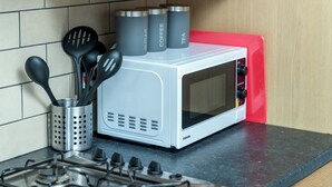 A kitchen with a white microwave, a red cutting board, and stainless steel containers labeled with food items. - Crawley Stainer 1-bedroom With Parking and Garden (Crawley)