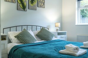 A neatly made bed with a teal blanket and two patterned pillows, a bedside lamp, and artwork on the wall. - Crawley Stainer 1-bedroom With Parking and Garden (Crawley)