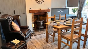 A cozy living room with a leather armchair, a wooden dining table set with plates and cups, a fireplace, and a large wall clock. - Luxury Seymour House With Spa, Gym & Lake District (Morecambe)