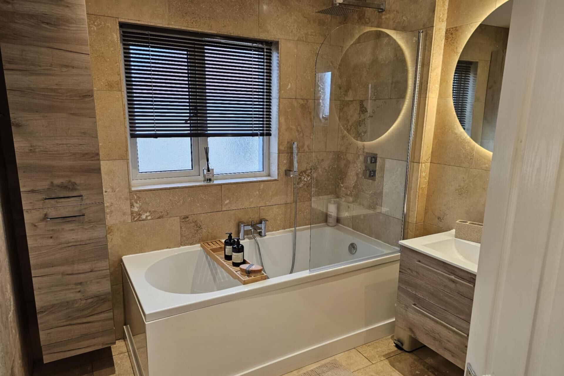 Une salle de bain moderne avec une baignoire sur pieds, une fenêtre avec des stores et un miroir rond.