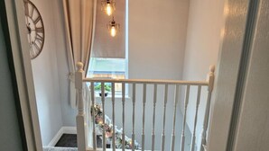 A staircase with a white railing, a clock on the wall, and hanging light fixtures. - Luxury Seymour House With Spa, Gym & Lake District (Morecambe)