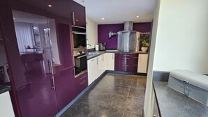 A modern kitchen with purple cabinets, a stainless steel range hood, and a bread maker on the counter. - Luxury Seymour House With Spa, Gym & Lake District (Morecambe)