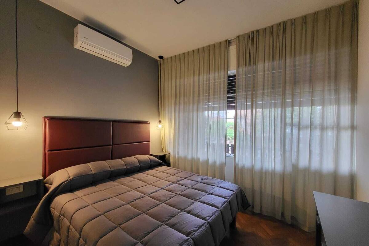 A bedroom with a bed, a nightstand, a lamp, and a window with curtains.