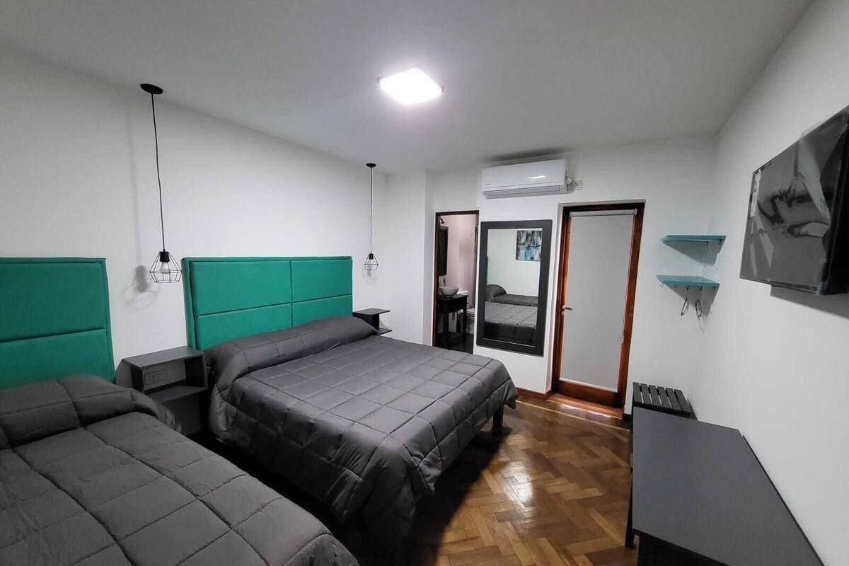 A room with two beds, a desk, a mirror, and a painting on the wall.