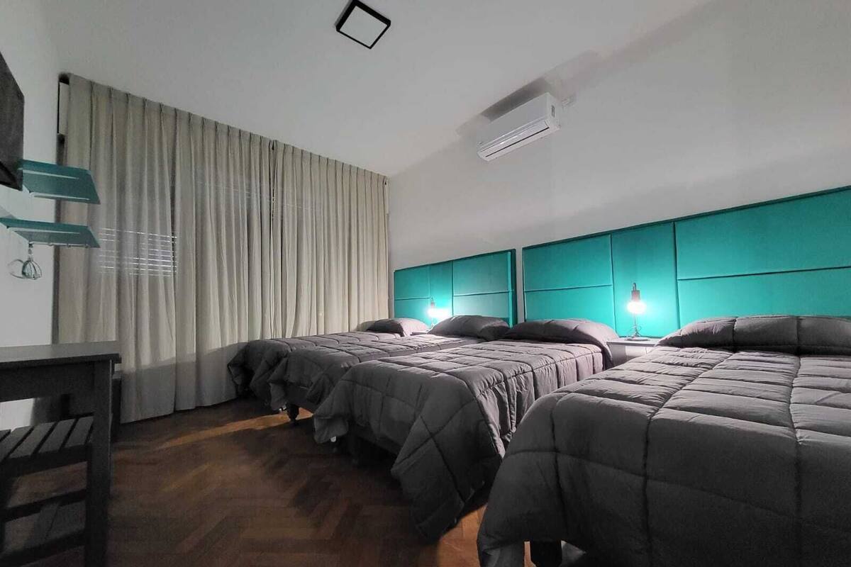 A hotel room with three beds, a desk, and a window with curtains.