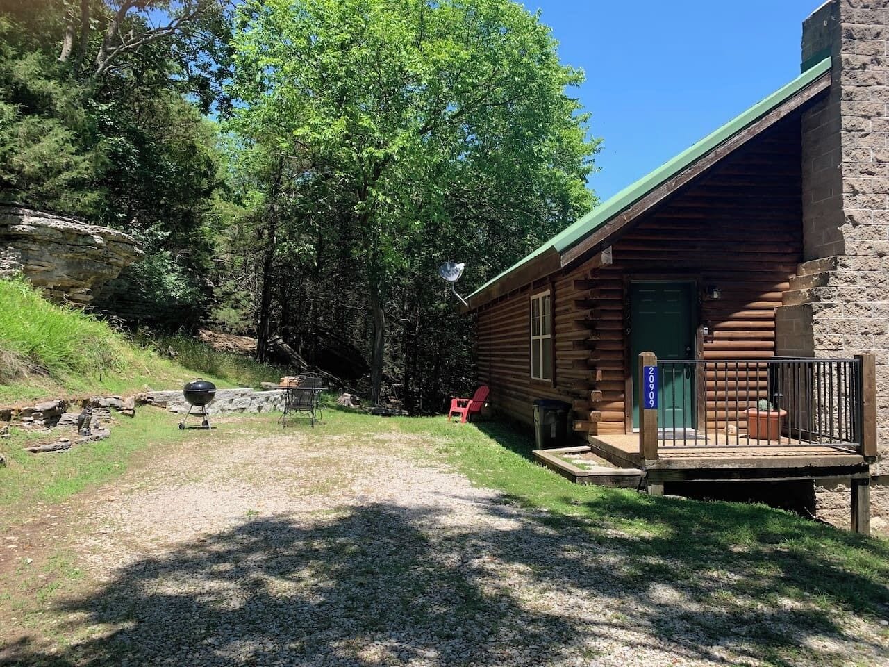 Une cabane rustique en rondins de bois, avec une porte verte, un porche et un chemin de gravier menant à l’entrée.