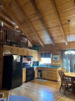 Interior de una cabaña de madera con cocina, comedor y una escalera.