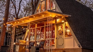 Una cabaña acogedora con un porche cubierto, ventanas amplias y una chimenea.