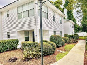 A two-story residential building with a white exterior, a visible address sign, and a well-maintained front yard with hedges and mulch. - La Vie Insulaire -optional BIKES–Walk 2 Redfern Village, shops, and restaurants! (St. Simons Island)