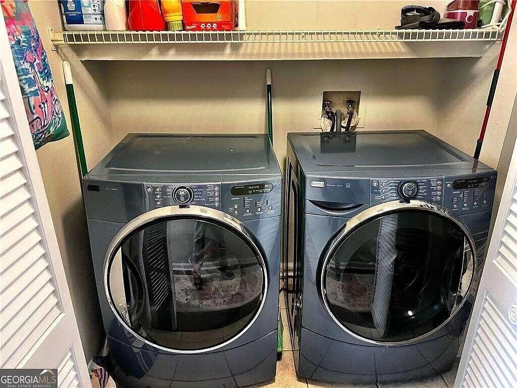 Two front-loading washing machines in a laundry room with a shelf above containing various items.
