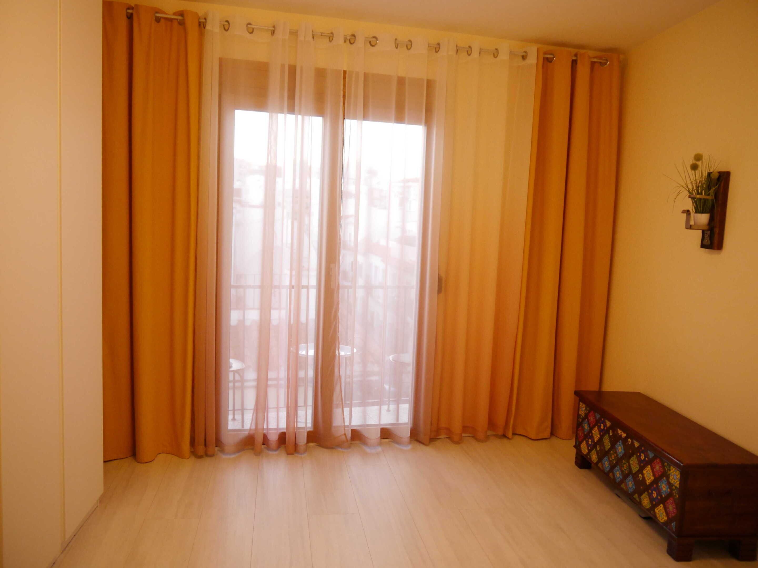 A room with large windows covered by sheer curtains, a wooden bench, and a small potted plant on the wall.