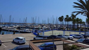 A marina with numerous boats docked, a parking area with cars, and palm trees along the waterfront. - Guadiana Sol (Estepona)