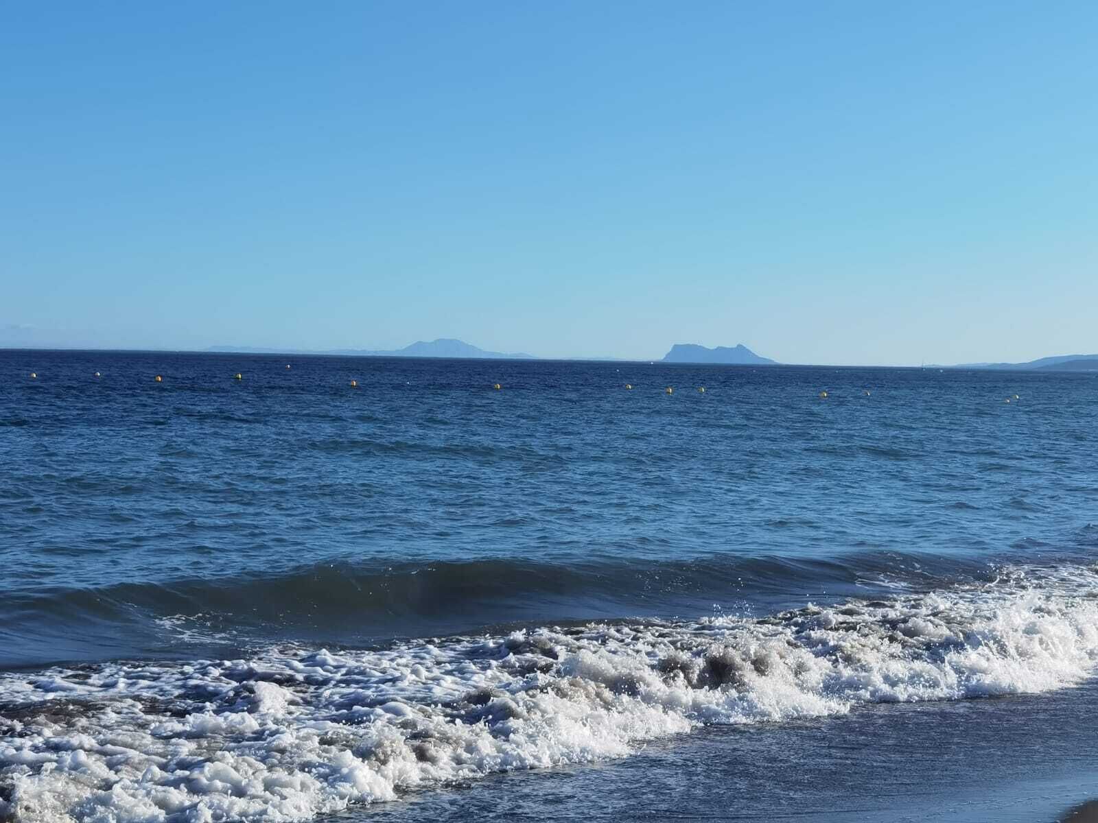 A coastal view with waves crashing onto the shore and a distant mountain range.