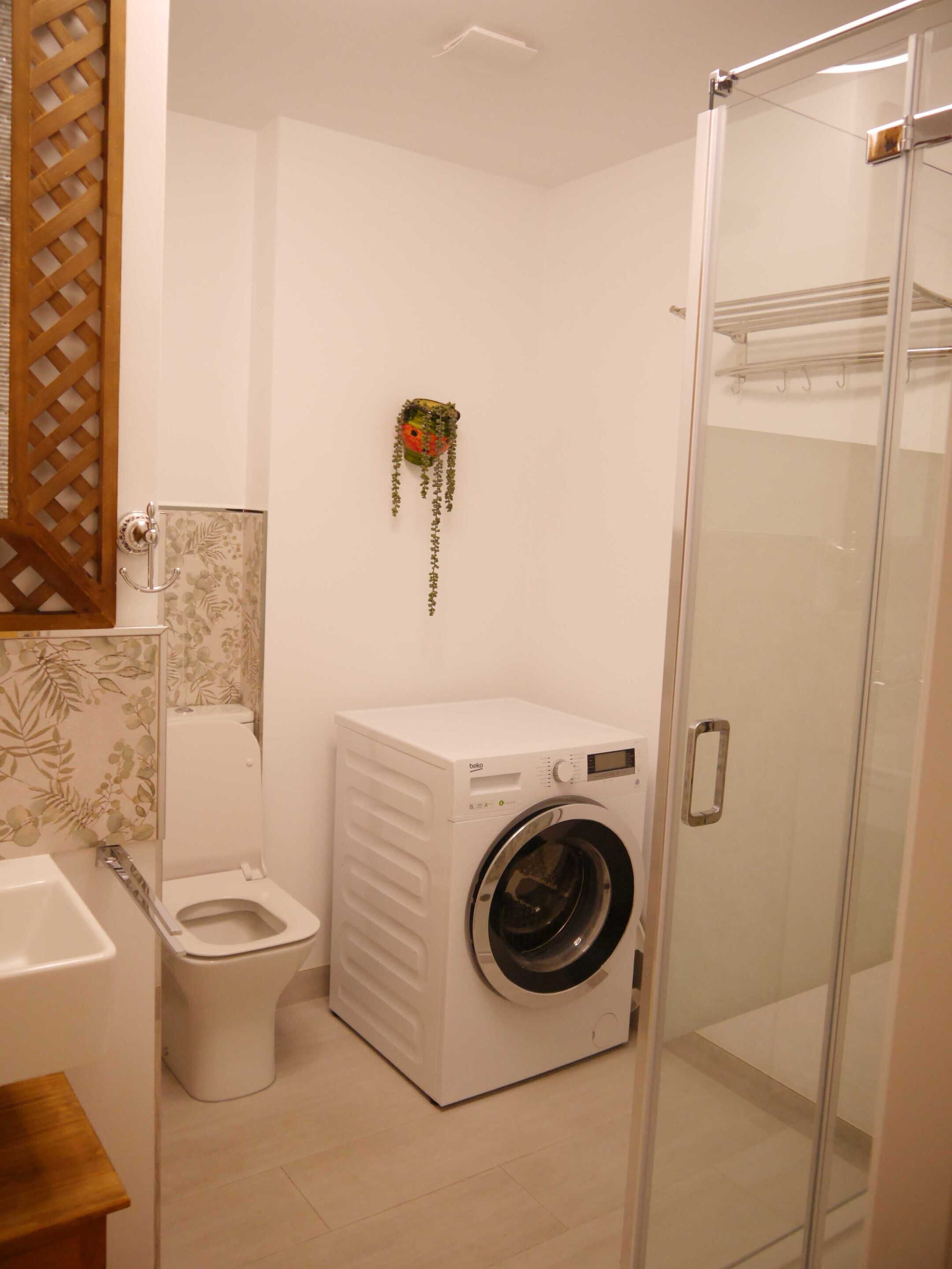 A compact bathroom with a washing machine, toilet, and glass shower enclosure.