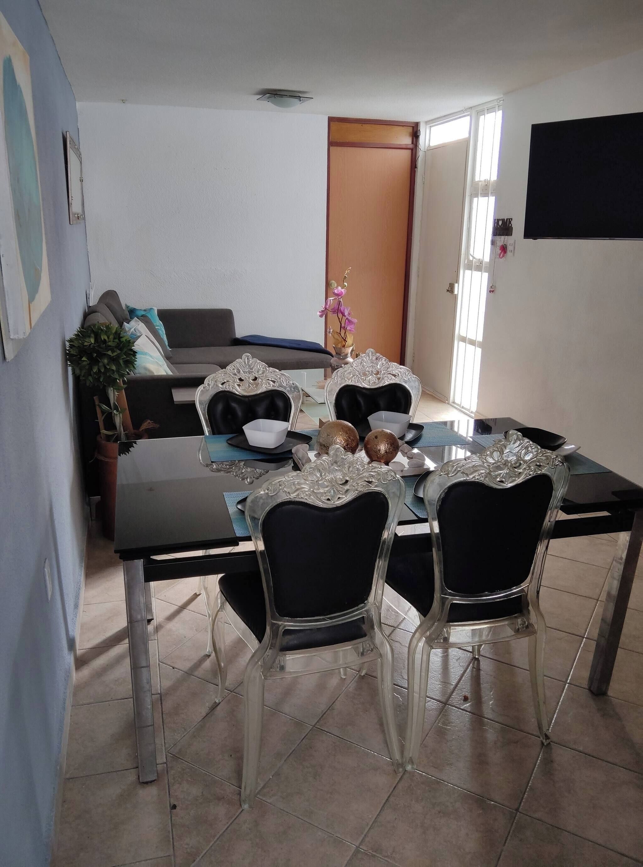 Un comedor con una mesa de vidrio, sillas negras y un florero con flores.