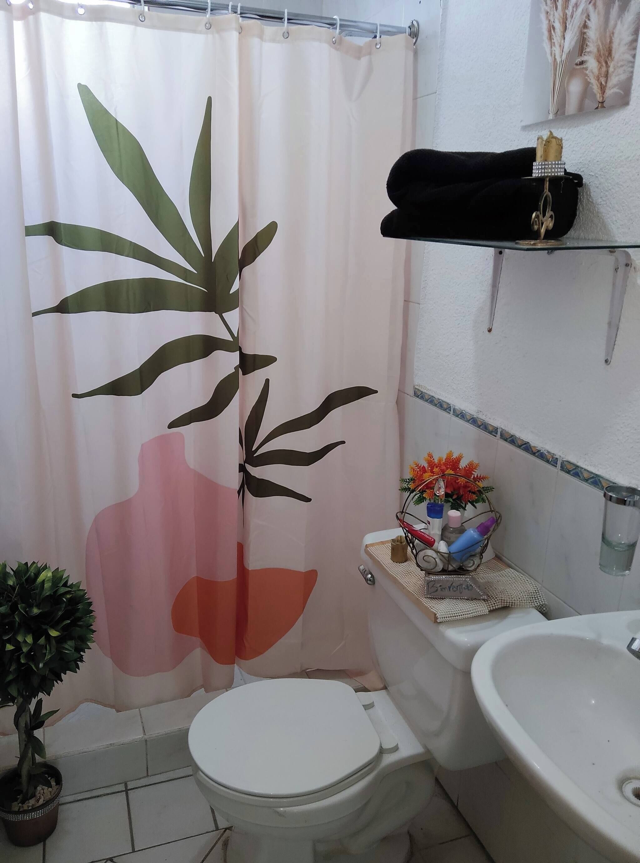 Baño con inodoro, lavabo y cortina de ducha con un diseño de planta grande.