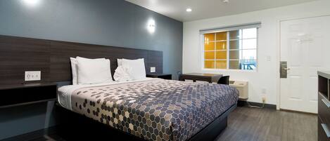 A modern hotel room with a large bed, a desk, and a window with a view.