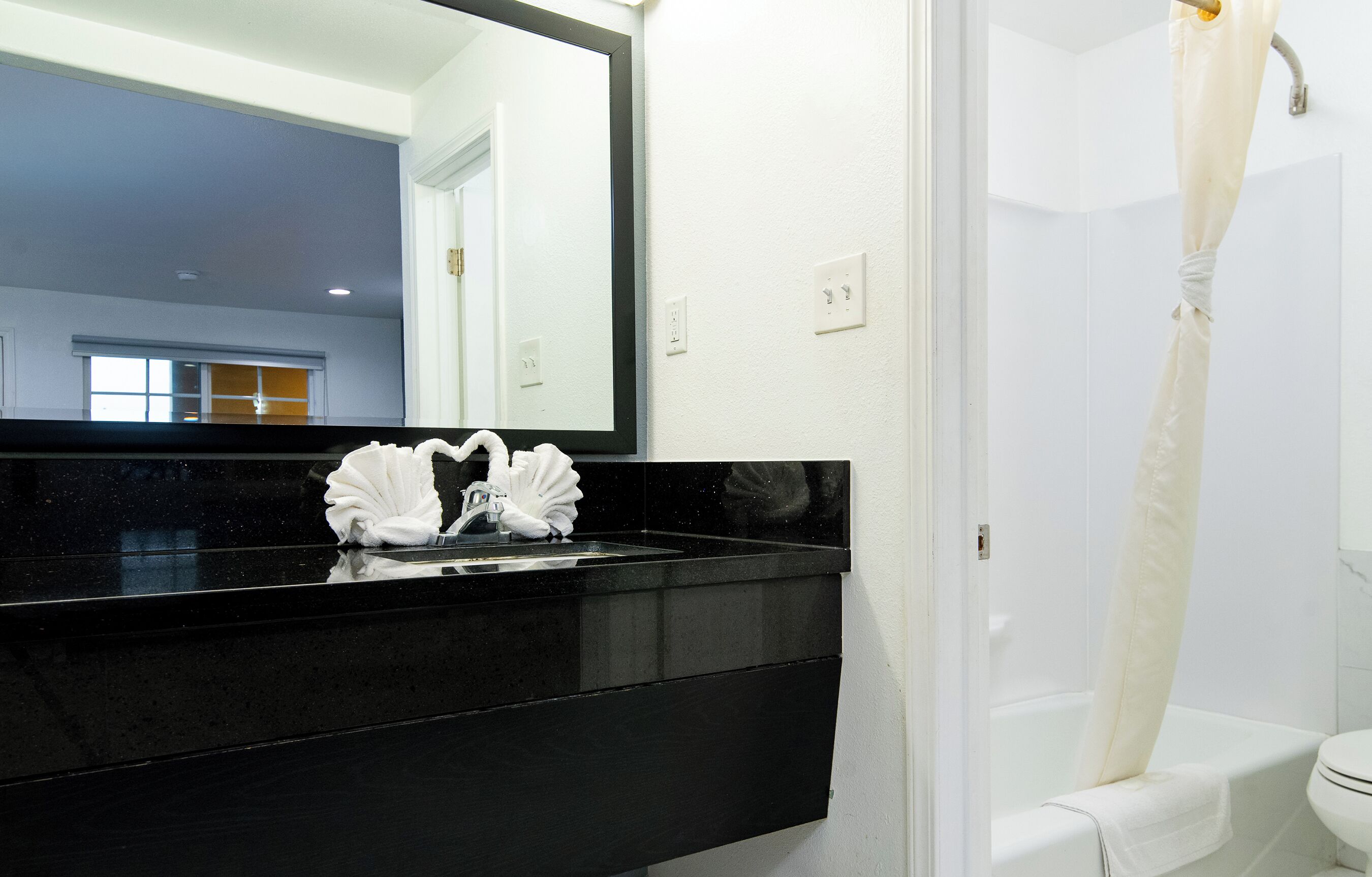 A modern bathroom with a black countertop sink, a large mirror, and a white shower curtain.