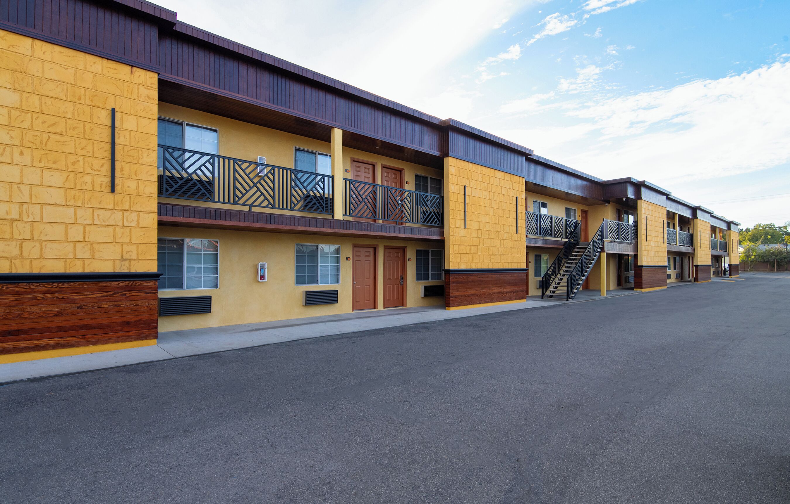 A multi-story motel with a yellow facade, balconies with metal railings, and a central staircase.