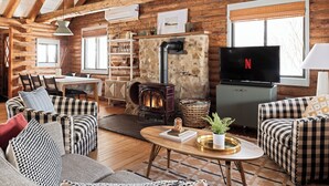 A cozy log cabin interior with a stone fireplace, a television, and checkered furniture. - Inground Pool, Hot Tub, Fire Pit at Large Log Cabin near Mohican State Park (Butler)