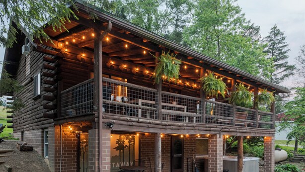 A log cabin with a balcony, outdoor seating, and string lights. - Inground Pool, Hot Tub, Fire Pit at Large Log Cabin near Mohican State Park (Butler)