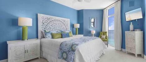 A bedroom with a bed, nightstands, a ceiling fan, a window with curtains, and a television.