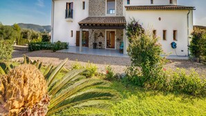 A two-story house with a stone facade, a covered porch, and a garden with tropical plants. - Spacious Villa With Infinity Pool (Son Servera)