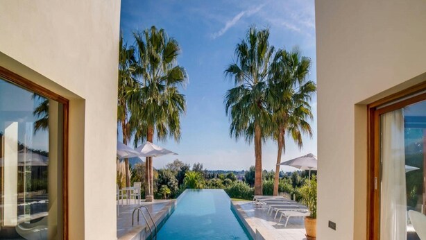 A swimming pool with clear blue water, surrounded by palm trees and a view of the landscape. - Spacious Villa With Infinity Pool (Son Servera)