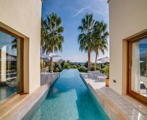 A swimming pool with clear blue water, surrounded by palm trees and a view of the landscape. - Spacious Villa With Infinity Pool (Son Servera)