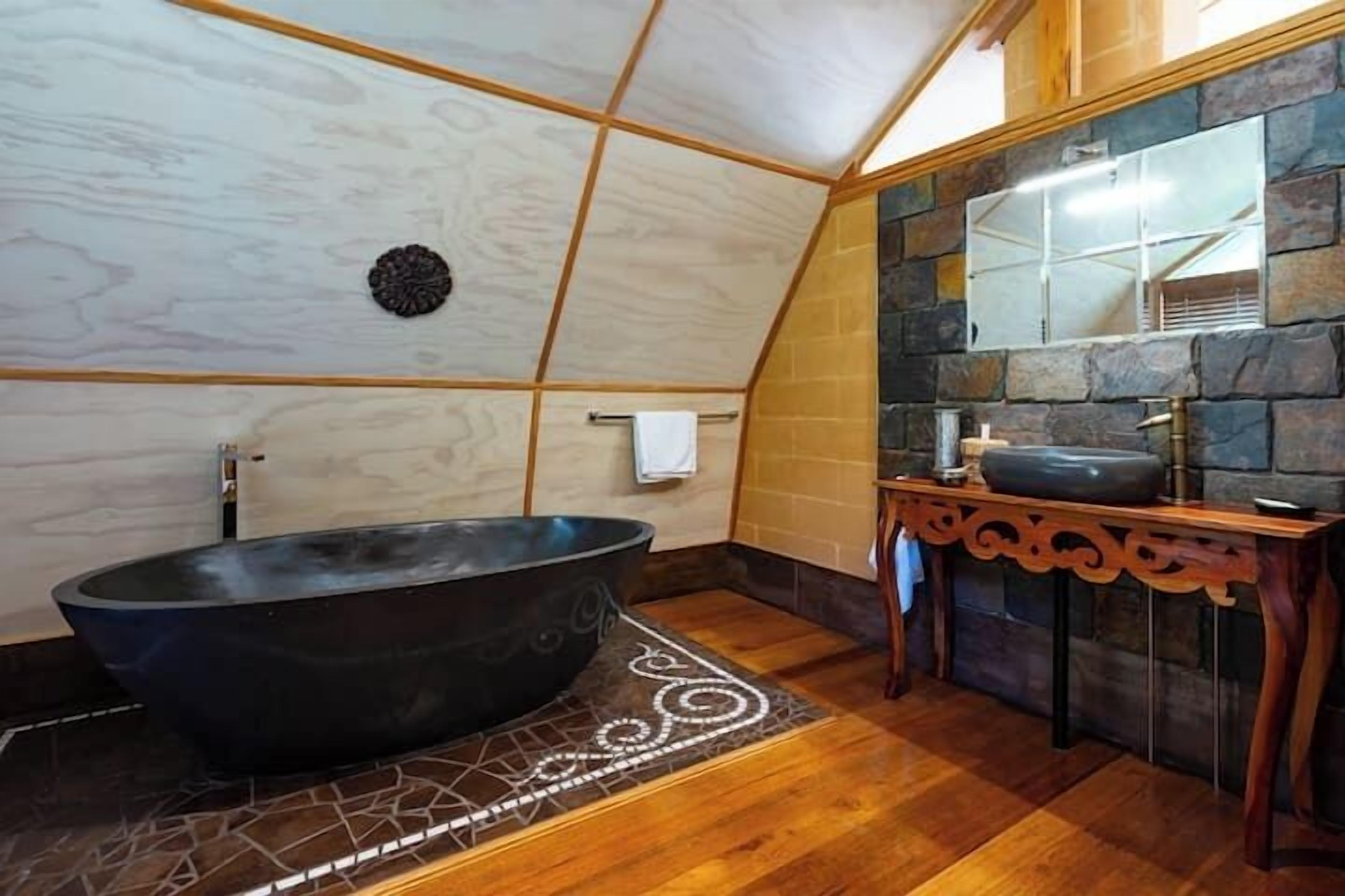 Ein Badezimmer mit freistehender Badewanne, einem Holzkosmetikschrank mit Waschbecken und einer Steinwand.