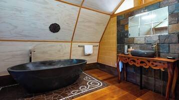 Ein Badezimmer mit freistehender Badewanne, einem Holzkosmetikschrank mit Waschbecken und einer Steinwand.