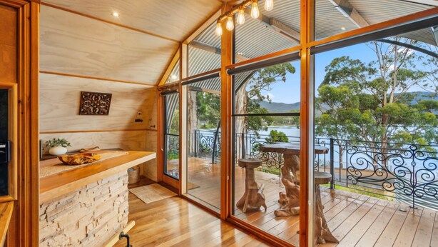 A wooden interior with a stone wall, a wooden counter, and a view of a deck with outdoor furniture. - Sanctuary Bruny Island - Dome 1 (suitable for two guests) (Adventure Bay)
