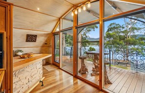 Un intérieur en bois avec un mur en pierre, un comptoir en bois et une vue sur une terrasse aménagée avec du mobilier d’extérieur.
