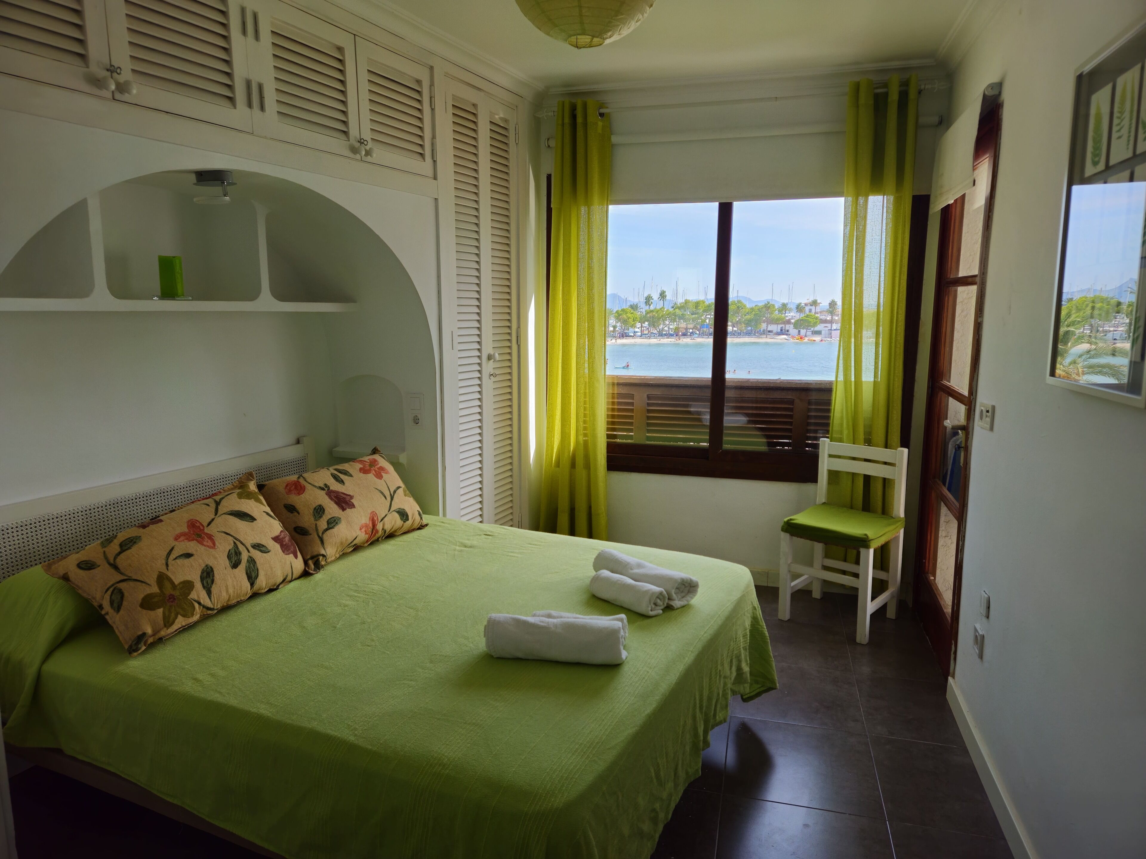 Una habitación de hotel con una cama, una silla, una ventana con vista a la playa y una repisa sobre la cama.