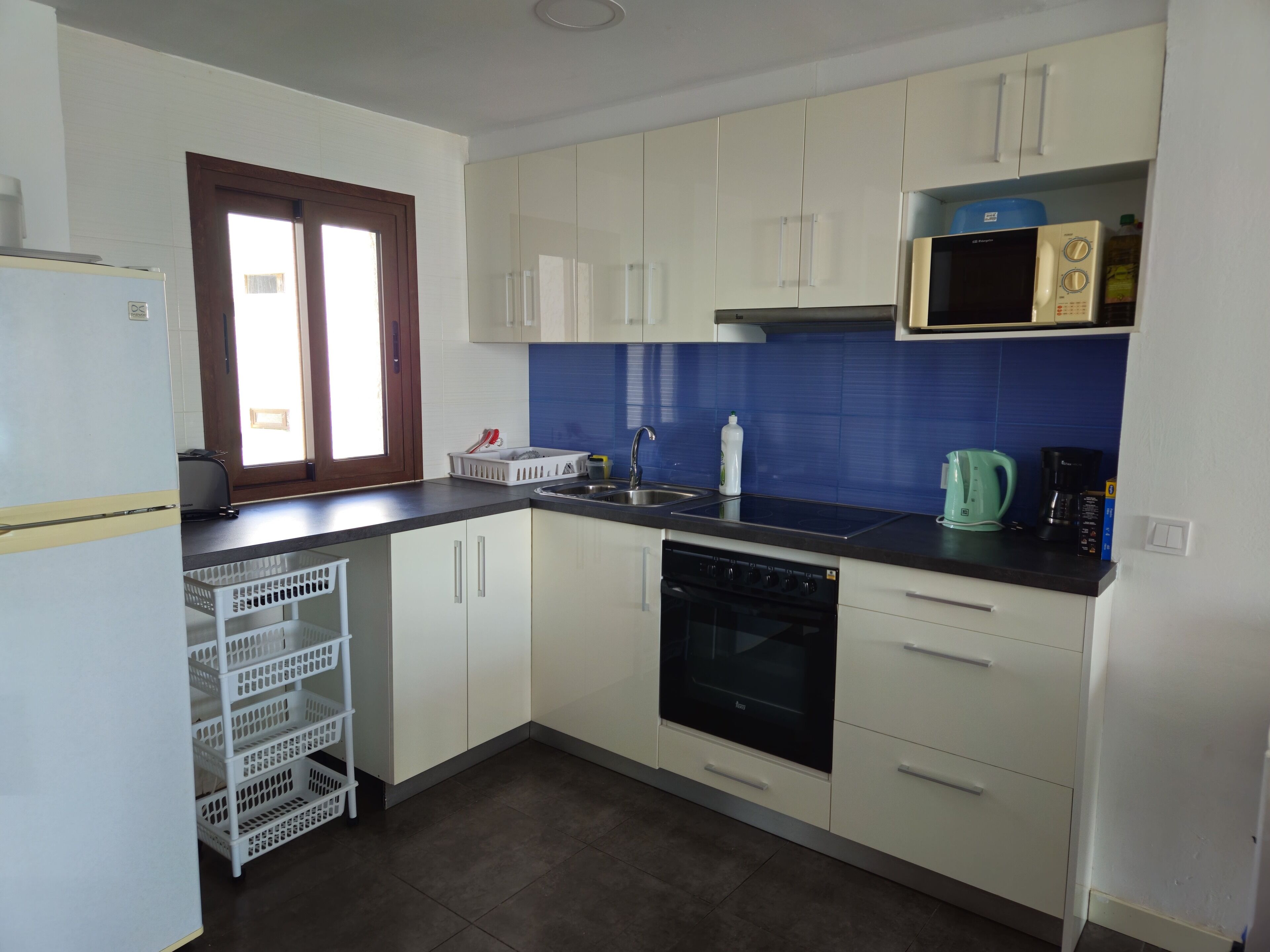 A compact kitchen with white cabinets, a black dishwasher, a microwave, and a kettle.