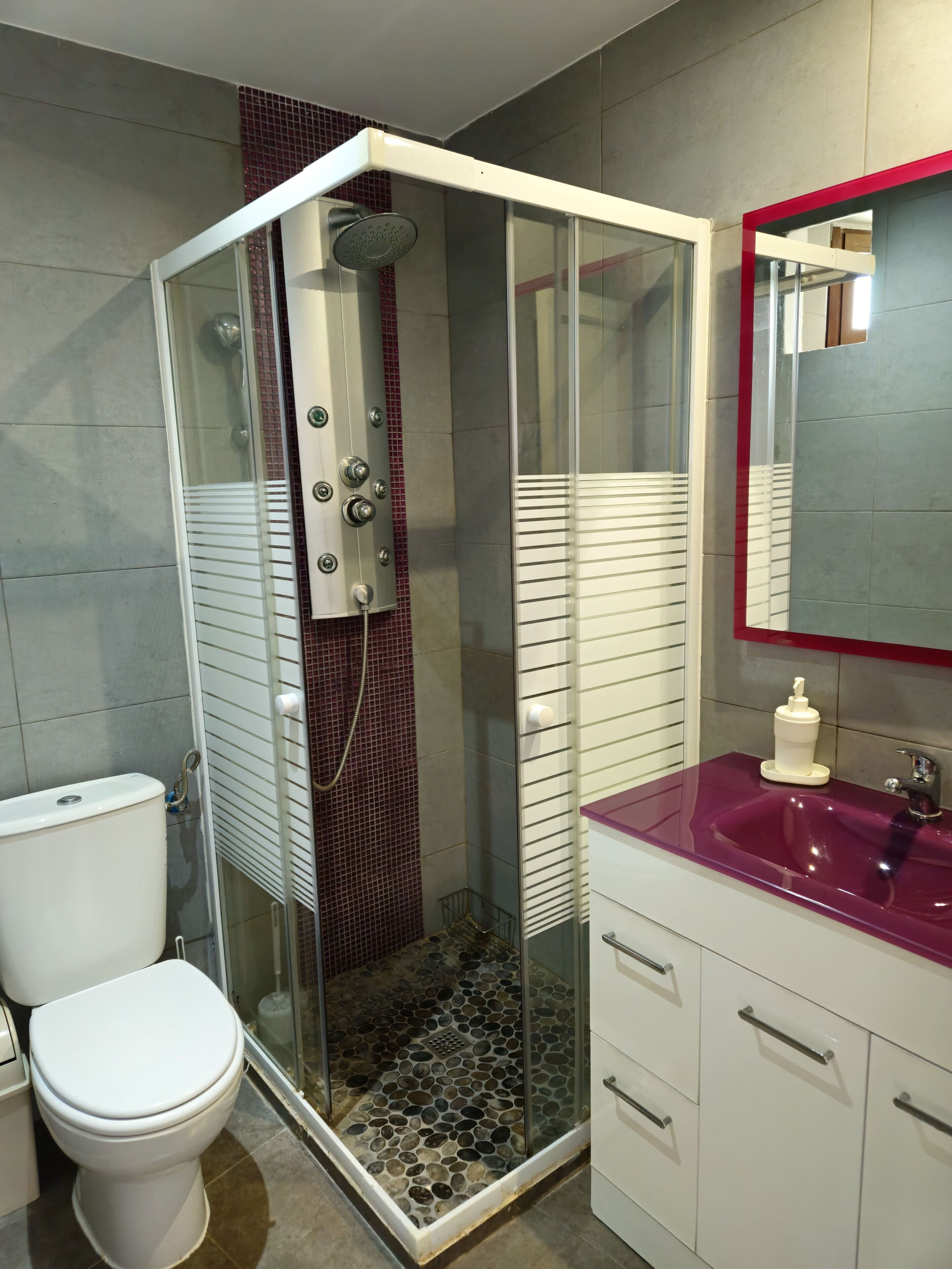Et moderne badeværelse med en glasafskærmet bruseniche, et hvidt toilet og en vaskebord med en lilla vask.