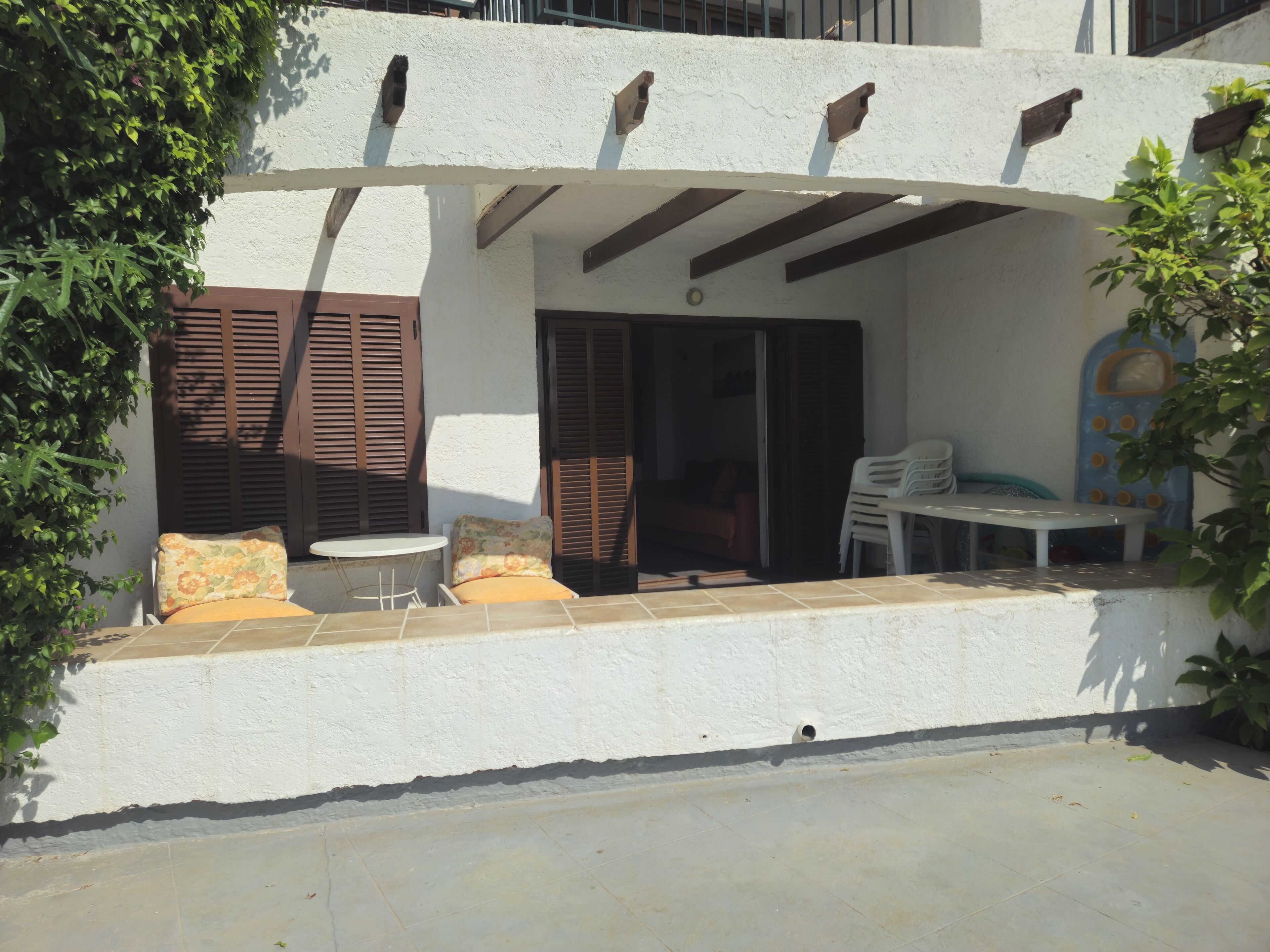 A covered outdoor seating area with a table and chairs, a small window, and a door leading inside.
