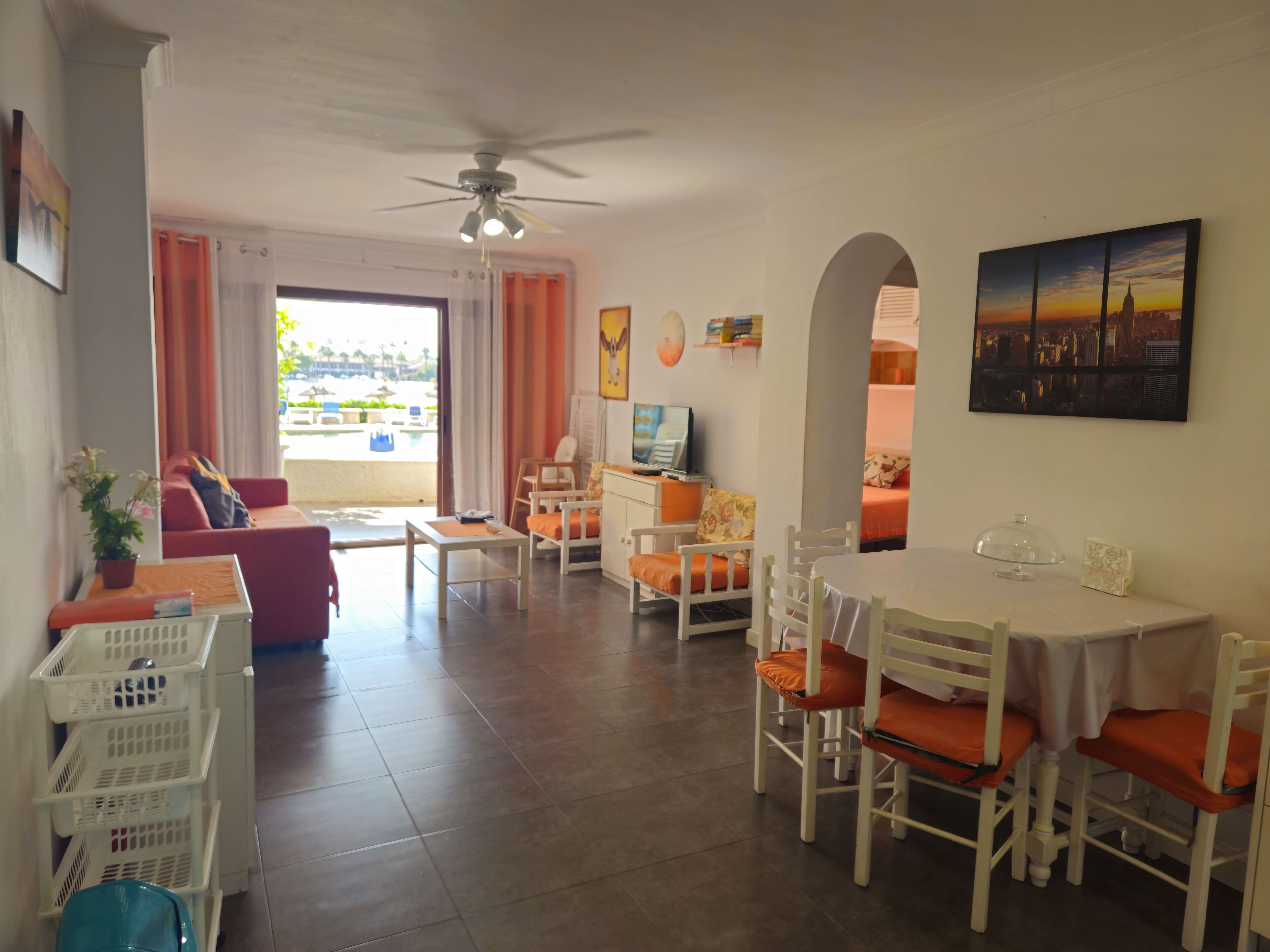 A hotel room with a dining area, a TV, a ceiling fan, and a view of the outdoors.