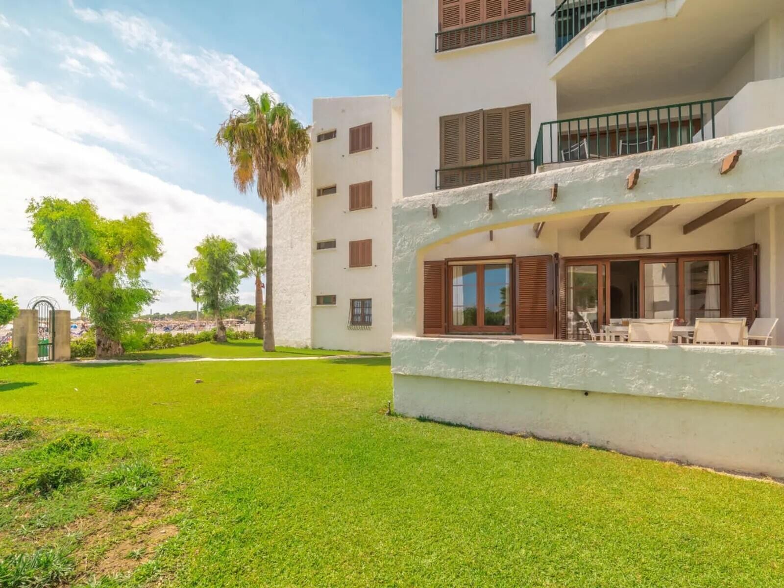 A multi-story building with balconies, a well-maintained lawn, and a palm tree.