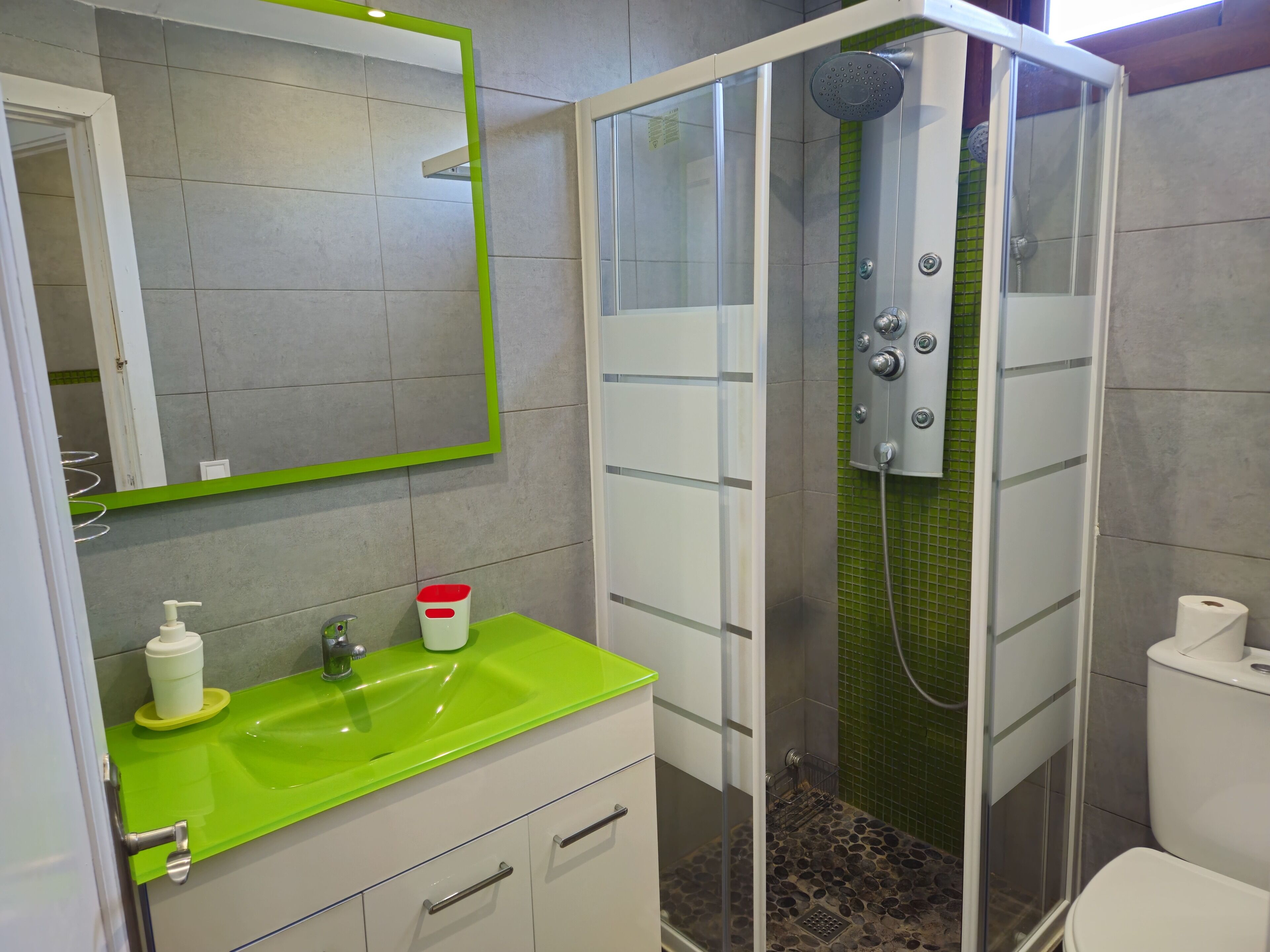 Une salle de bain avec un lavabo vert, des toilettes blanches et une douche fermée par une paroi de verre.