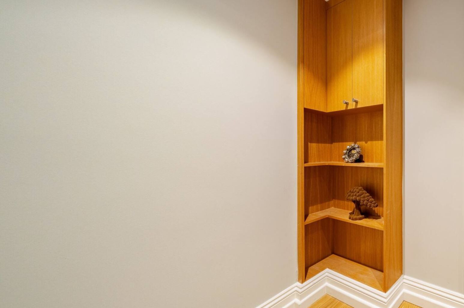 A corner with a wooden built-in shelf unit against a plain wall.