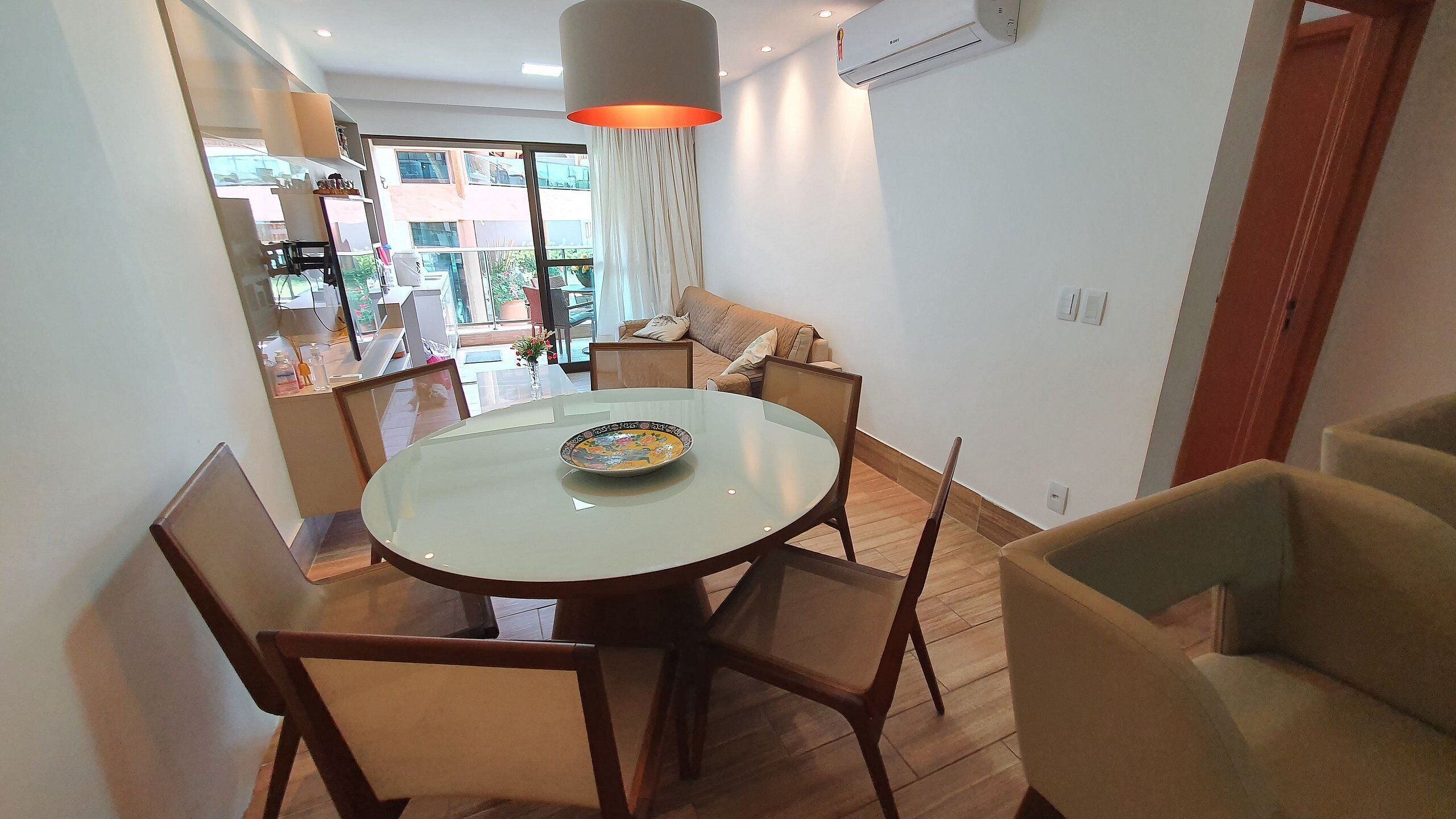 Un espace repas comprenant une table ronde, des chaises, un luminaire suspendu et une vue sur un balcon.
