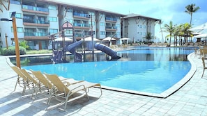 Una piscina con lettini, uno scivolo e un edificio sullo sfondo con balconi.