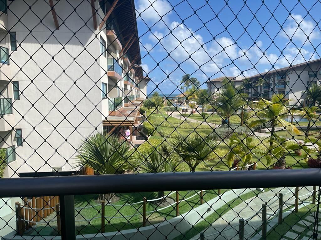 A chain-link fence with a view of a building and a green lawn with palm trees.