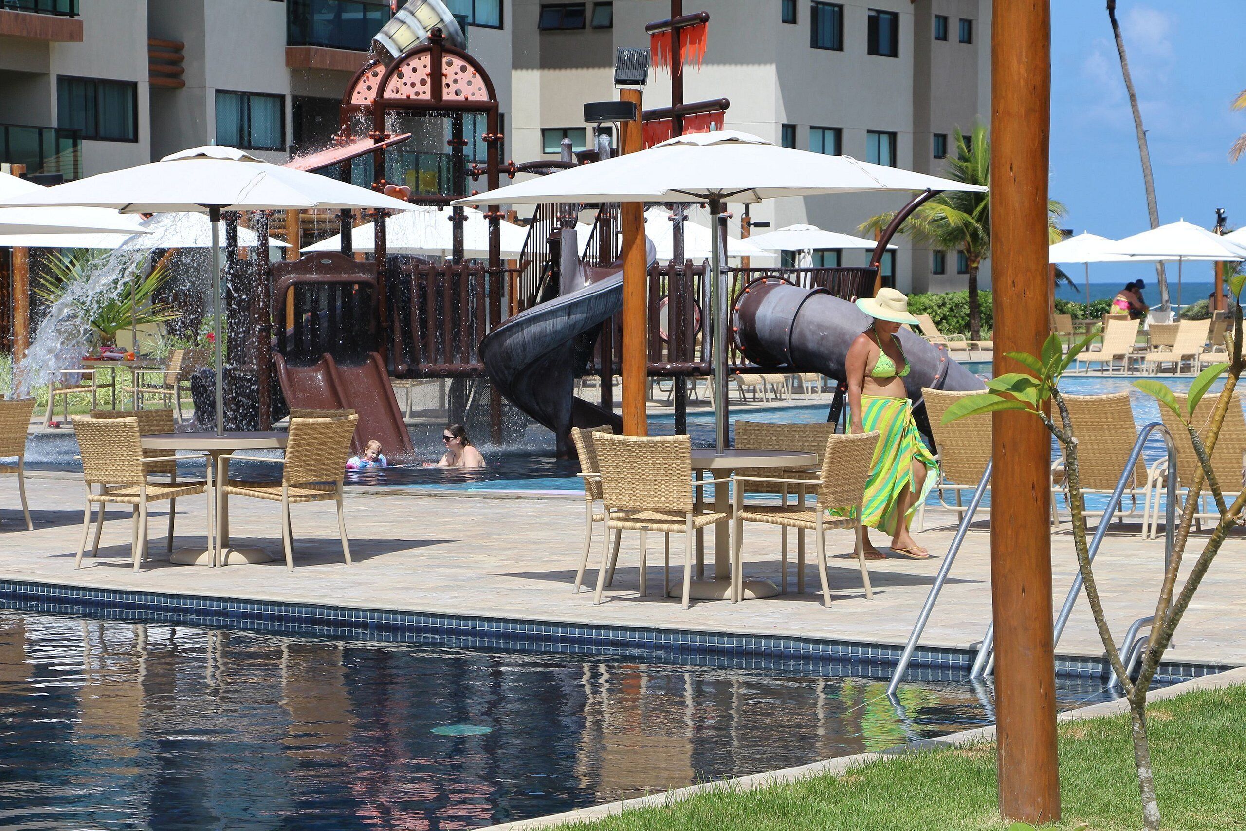 A pool area with a water slide, lounge chairs, and umbrellas.